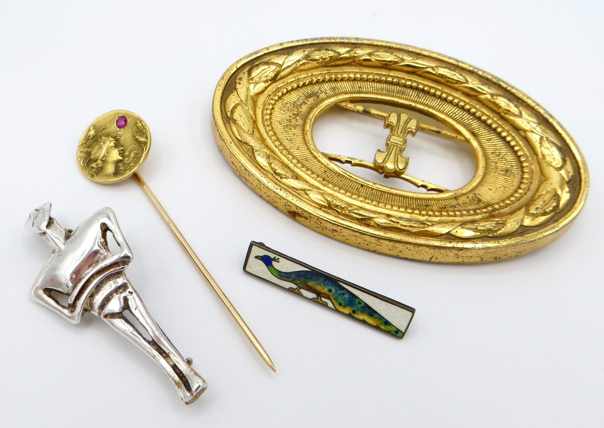 L-R: A sterling silver stylized brooch, a gold and ruby stick pin, and enamel bar brooch and a vintage kilt pin.