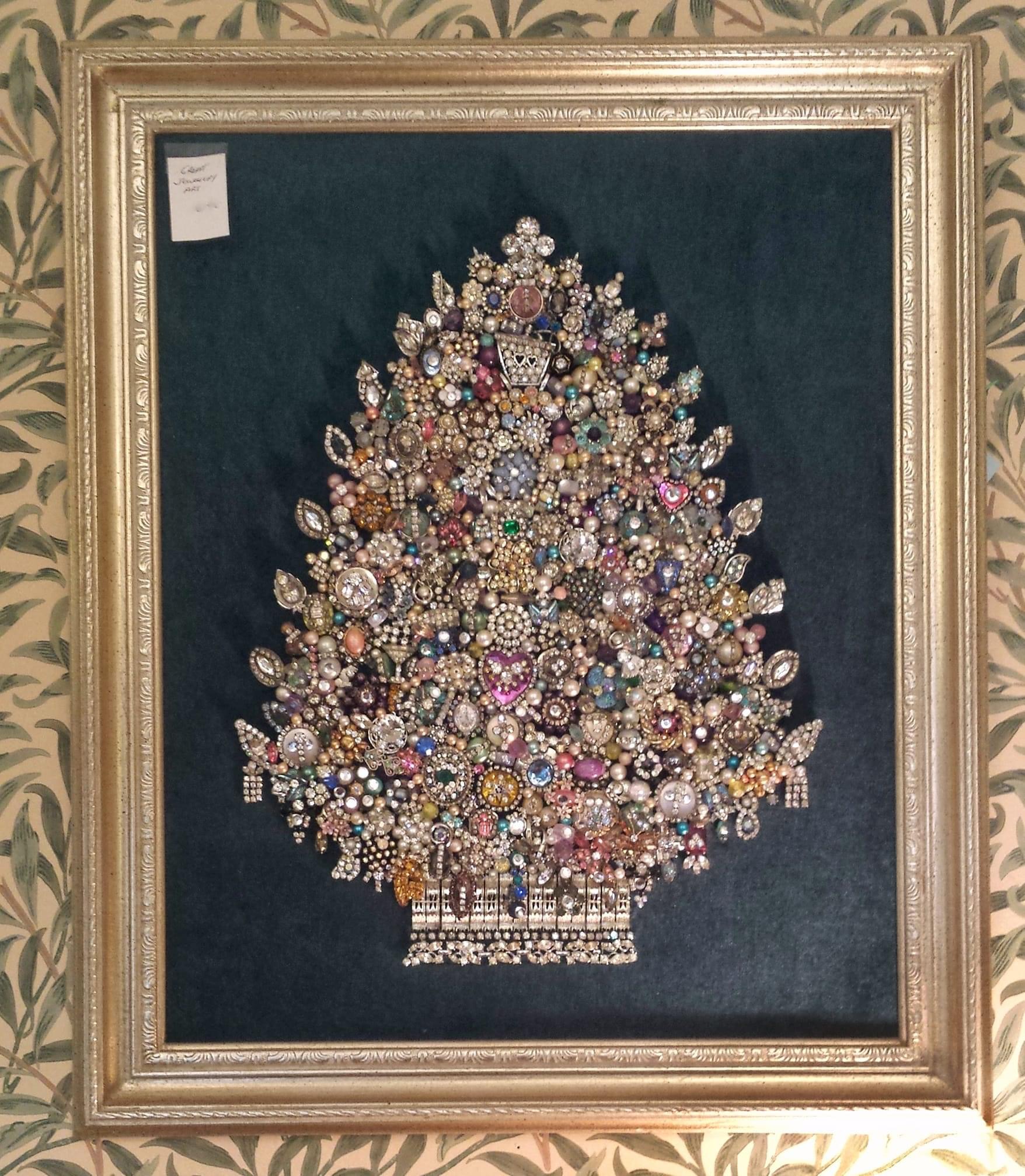 A framed picture of a Christmas tree. The tree itself is composed of vintage jewelery components. 