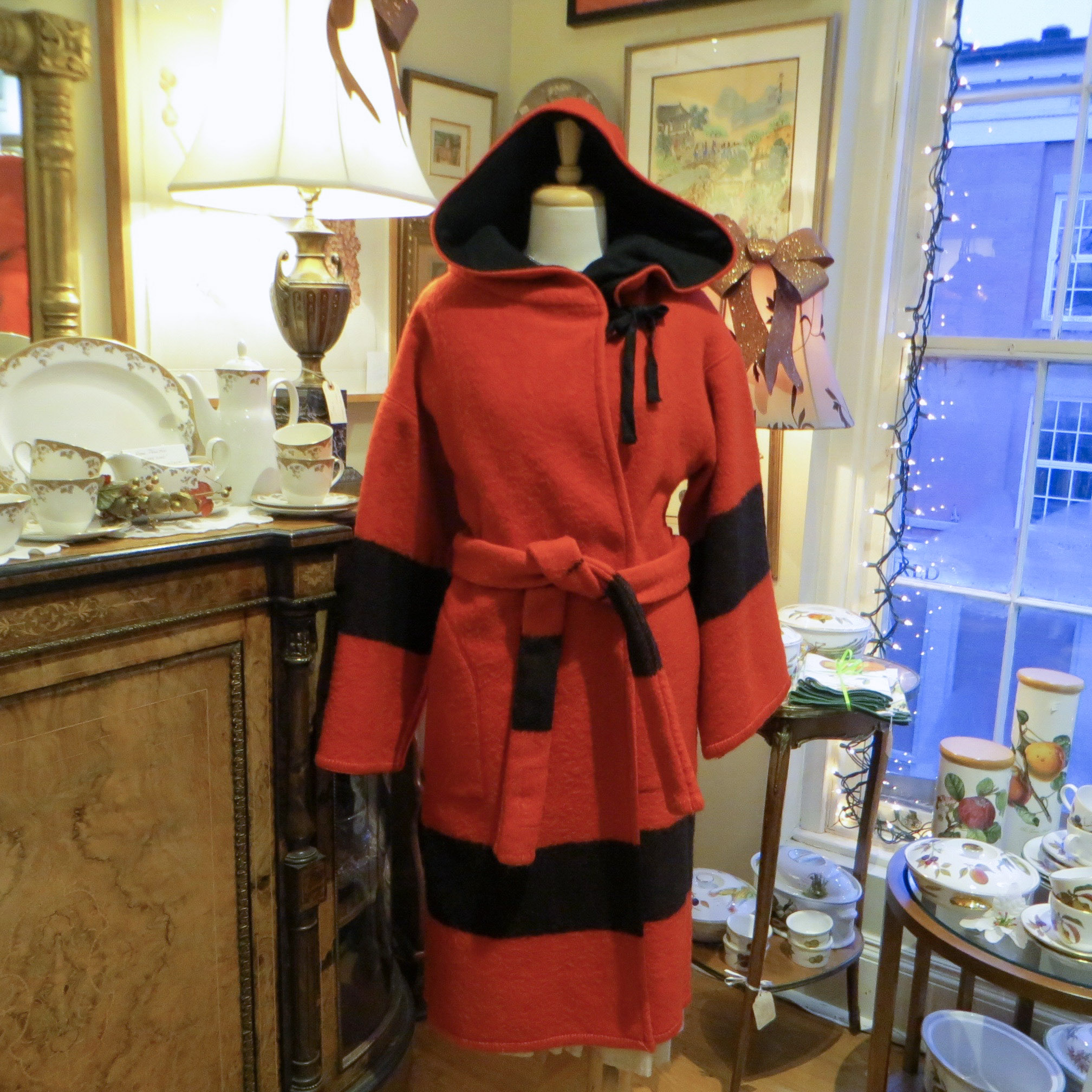 Eaton's Point blanket coat. A red hooded coat with black stripes is worn by a mannequin. The background shows an interior wall on the left and a window on the right. 