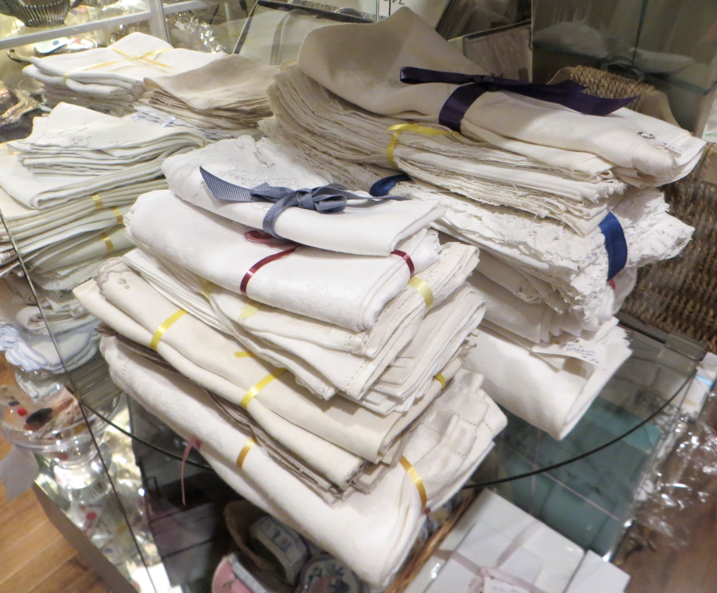 Piles of folded white linen napkins sit atop a glass shelf.