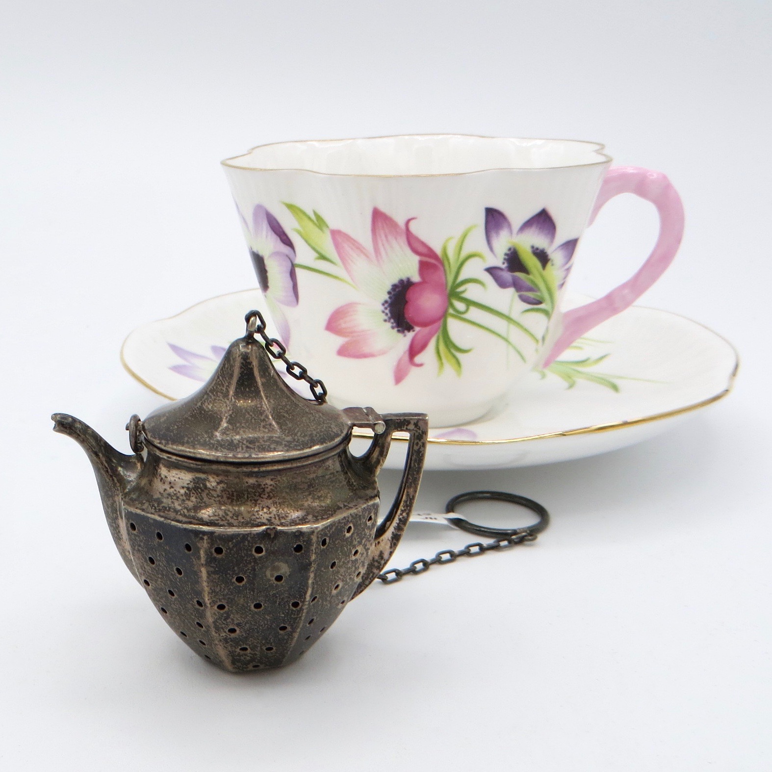 sterling silver infuser in the shape of a teapot, with a pink and white tea cup in the background