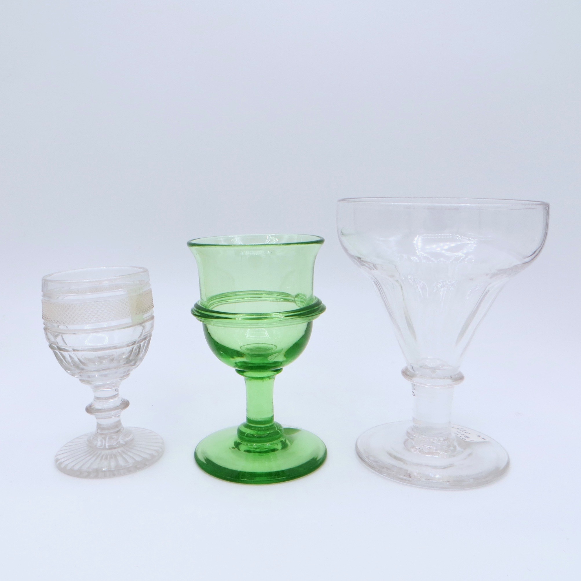 Three glasses of varying sizes and designs. The centre glass is green, while the other two are clear.