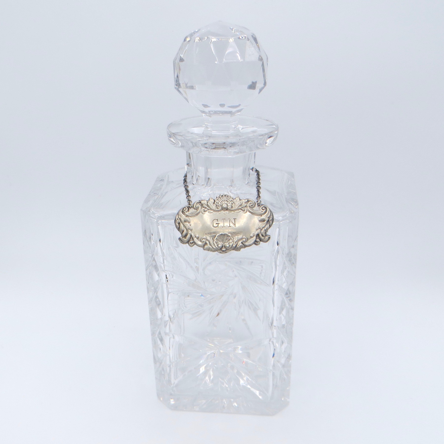 A square cut crystal decanter with a round stopper and a silver label reading "gin"